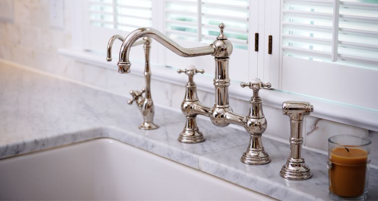 A steel kitchen faucet with a marble countertops.
