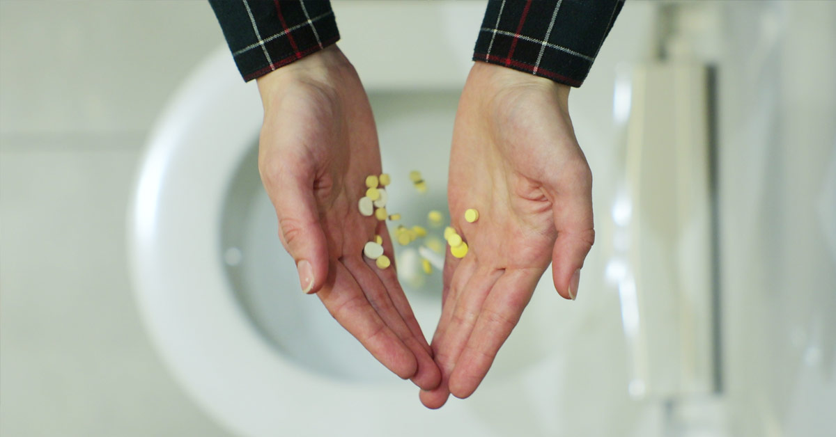 Hands dropping medication in the toilet.